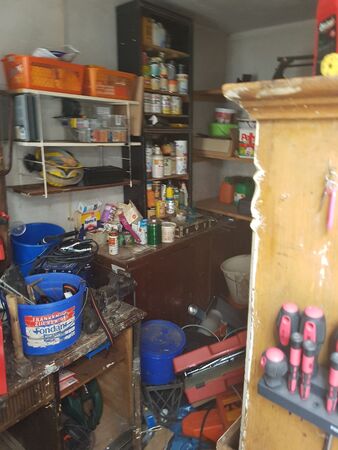 Unordentliche Werkstatt mit Regalen voller Werkzeuge, Farbe, Schraubendrehern und Zubehör.