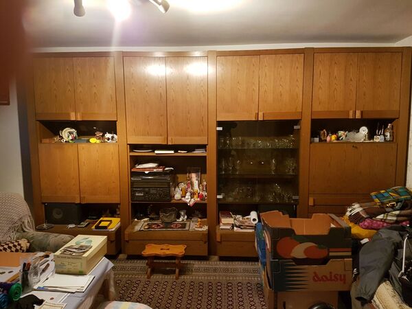 Großer, brauner Wohnzimmerschrank mit Glastüren, Dekoration, Kartons und Hausrat im Raum.